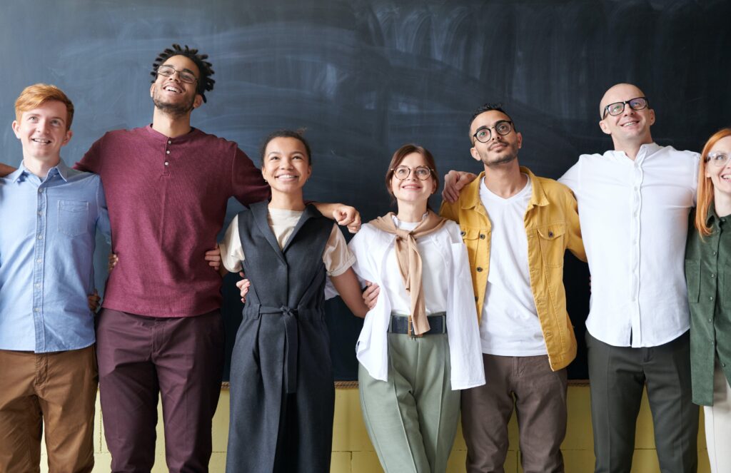 Seven people standing with their arms round each other in front of a blackboard