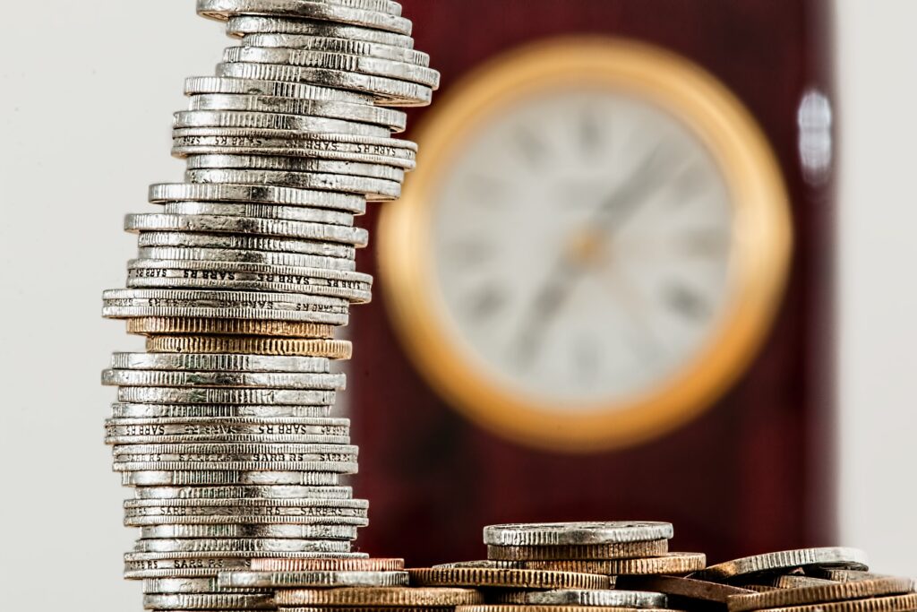 Close up photo of stack of coins with blurred clock in background